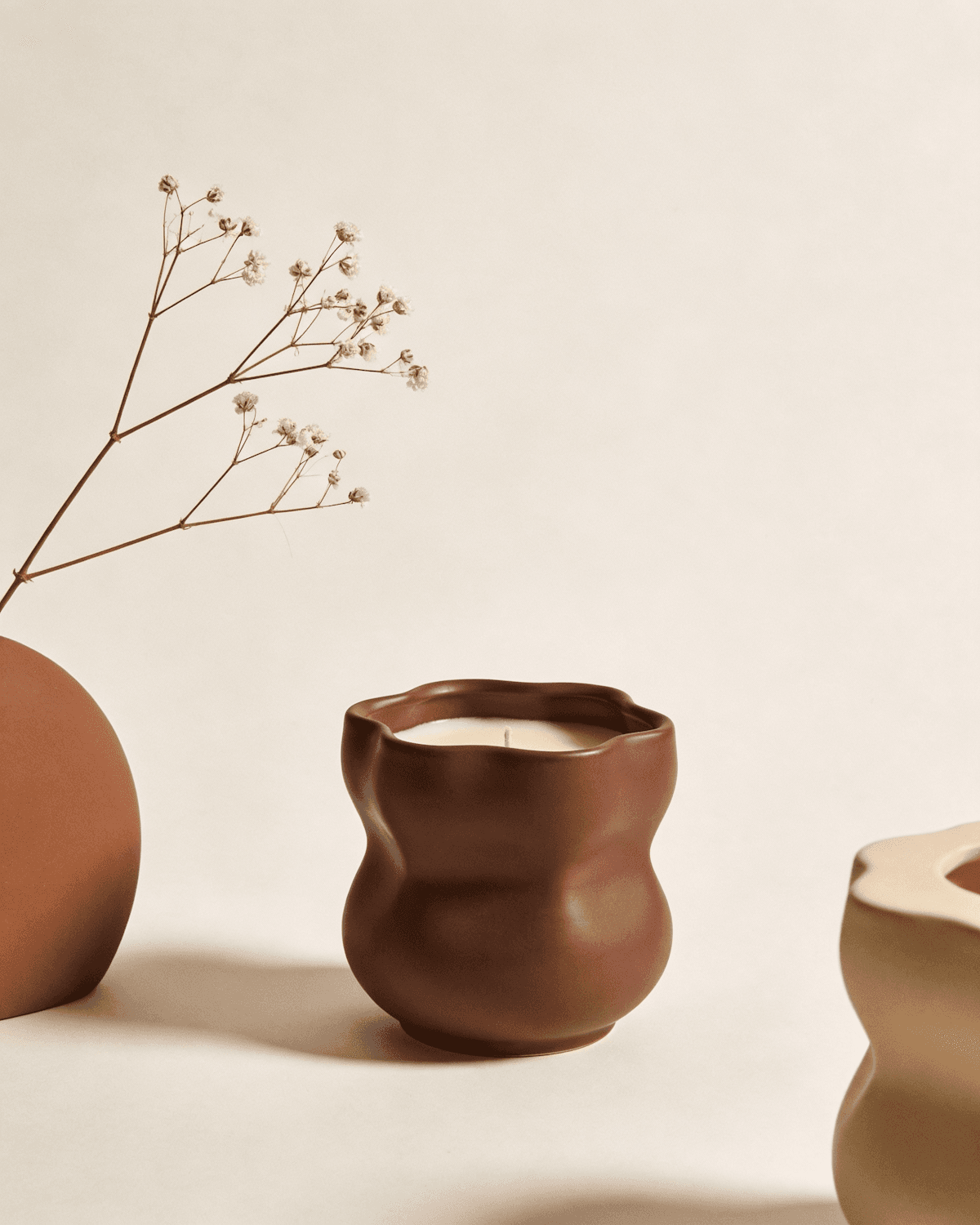 Brown wave ceramic candle beside a vase of dried flowers